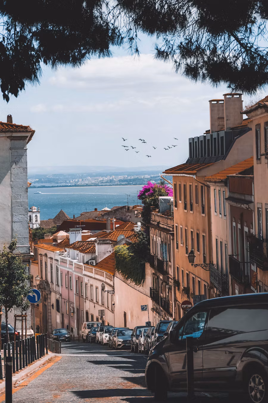 Sloping street lined with buildings, looking over the rooftops to the Tagus in Lisbon