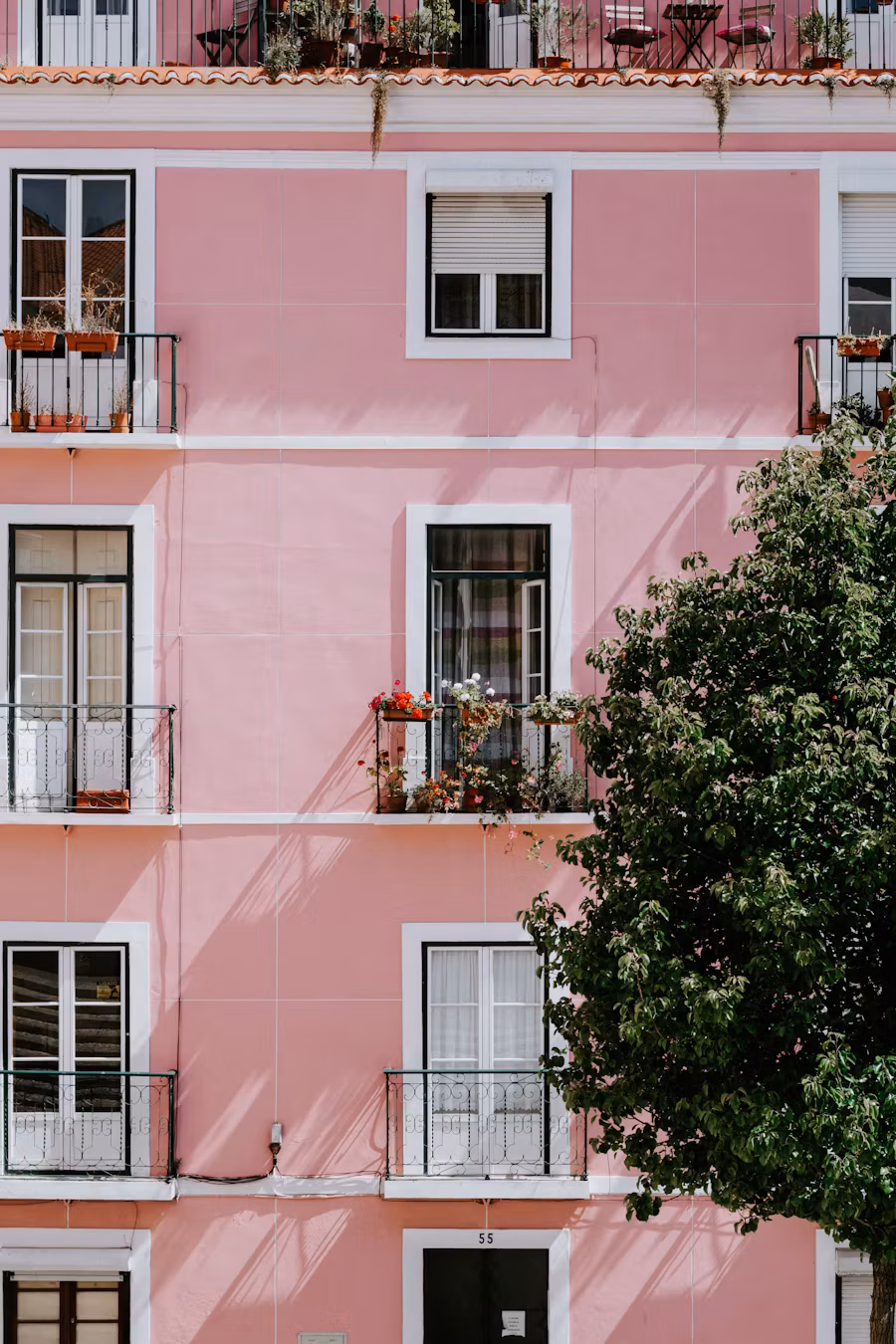 Pink residential facade in Lisbon with flower-filled balconies and a tree